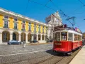 Czerwony tramwaj w Lizbonie, obok żółtego budynku z arkadami. Czy do Portugalii trzeba paszport? Nie, wystarczy dowód osobisty.