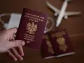 Dłoń trzyma paszport RP. W tle maseczka, samolot i kolejne paszporty, jakby przygotowania do podróży z urzędu wojewódzkiego w Kielcach.