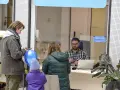 Rodzina czeka na obsługę w urzędzie paszportowym Piaseczno. Mężczyzna z telefonem i niebieskim balonem, kobieta z dzieckiem w fioletowej kurtce.