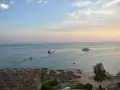 Spokojna plaża z leżakami i parasolami, statki na morzu. Czy wyjazd do Sharm El Sheikh jest bezpieczny? Widok sugeruje relaks.