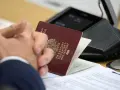 Pasport w rękach klienta w biurze paszportowym Myślibórz. Dokumenty i urządzenie do wideokonferencji na stole.