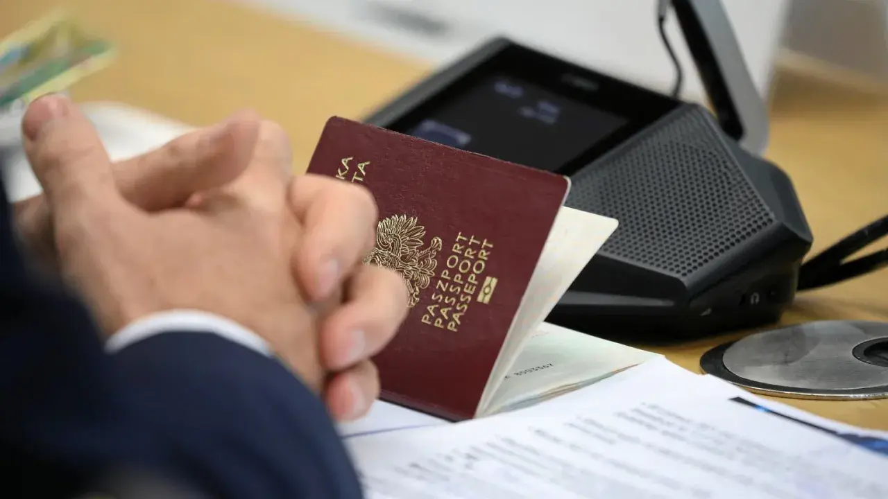 Pasport w rękach klienta w biurze paszportowym Myślibórz. Dokumenty i urządzenie do wideokonferencji na stole.