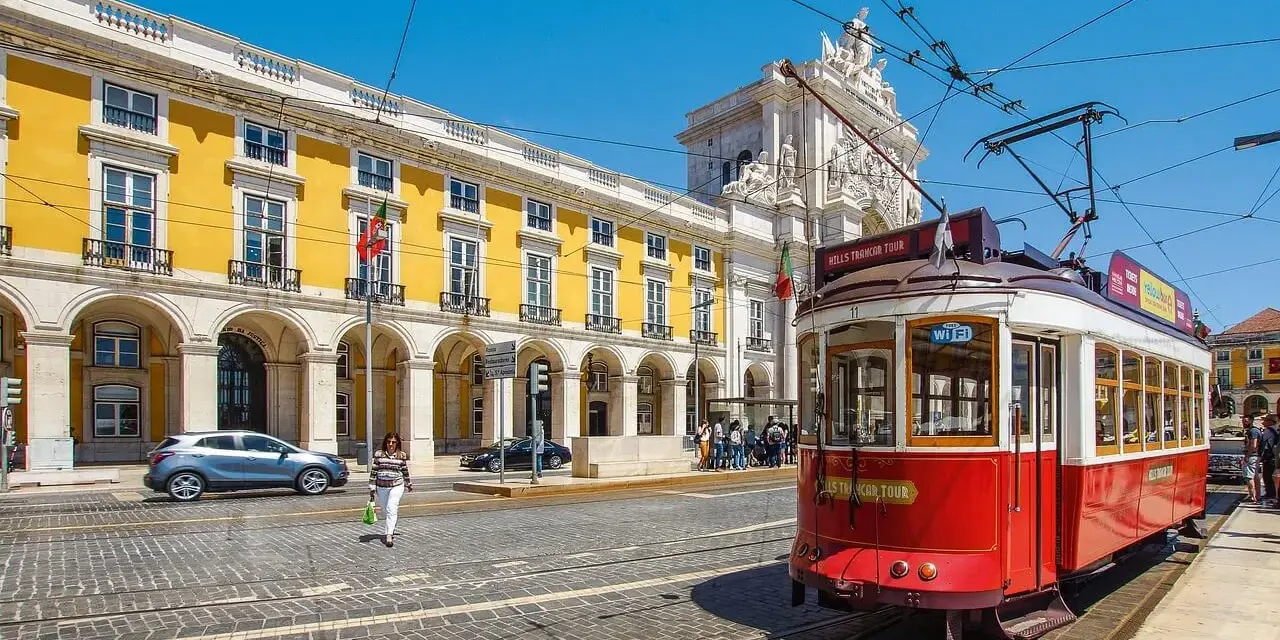 Czerwony tramwaj w Lizbonie, obok żółtego budynku z arkadami. Czy do Portugalii trzeba paszport? Nie, wystarczy dowód osobisty.