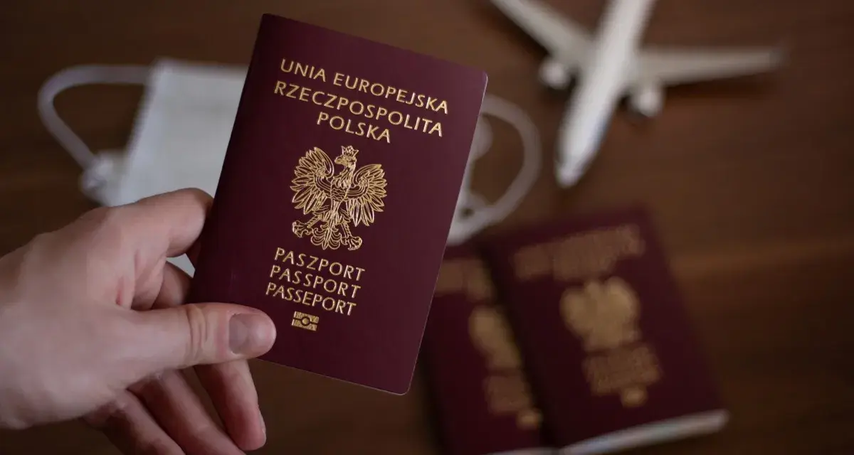 Dłoń trzyma paszport RP. W tle maseczka, samolot i kolejne paszporty, jakby przygotowania do podróży z urzędu wojewódzkiego w Kielcach.