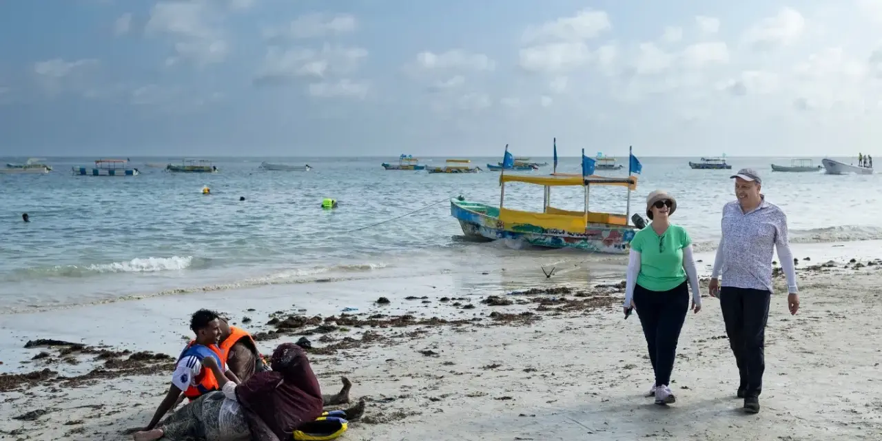 Spacerowery na plaży w Somalii, z łodziami na morzu. Czy Somalia jest bezpieczna? Turyści spacerują, podczas gdy lokalni mieszkańcy odpoczywają na piasku.