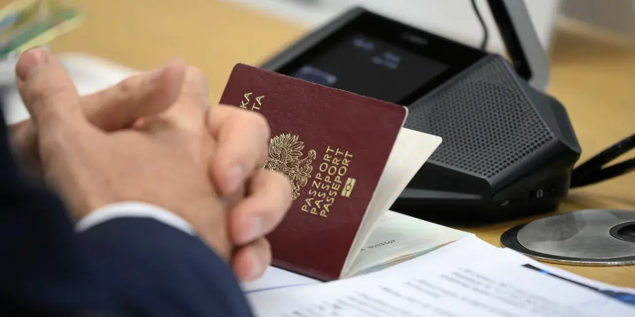 Pasport w rękach klienta w biurze paszportowym Myślibórz. Dokumenty i urządzenie do wideokonferencji na stole.