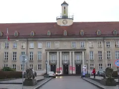 Elegancki budynek z zegarem na wieży, gdzie znajduje się urząd paszportowy Koszalin. Przed wejściem stoją lwy.