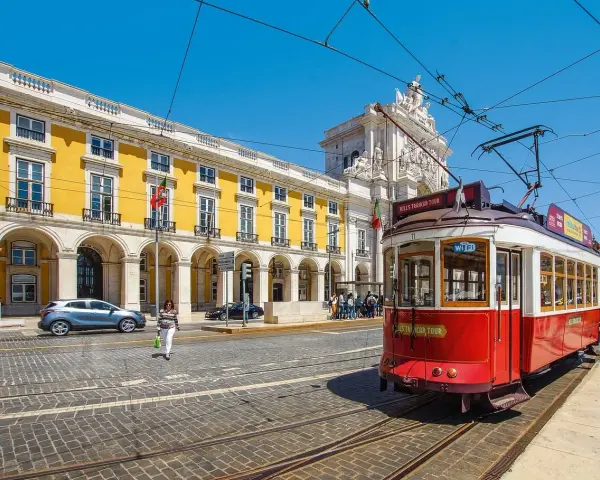 Czerwony tramwaj w Lizbonie, obok żółtego budynku z arkadami. Czy do Portugalii trzeba paszport? Nie, wystarczy dowód osobisty.