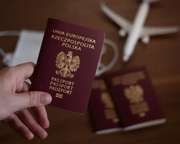 Dłoń trzyma paszport RP. W tle maseczka, samolot i kolejne paszporty, jakby przygotowania do podróży z urzędu wojewódzkiego w Kielcach.