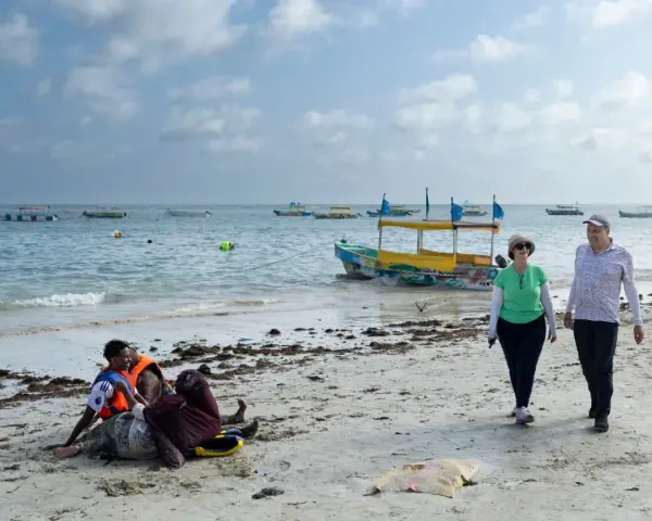 Spacerowery na plaży w Somalii, z łodziami na morzu. Czy Somalia jest bezpieczna? Turyści spacerują, podczas gdy lokalni mieszkańcy odpoczywają na piasku.