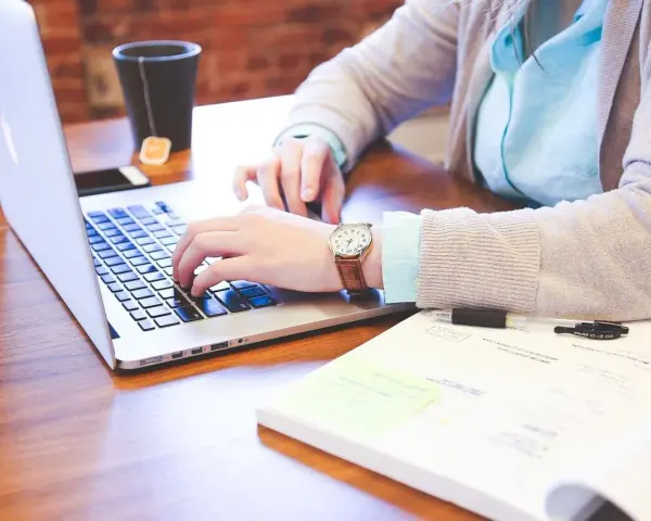 Kobieta pracuje na laptopie, szukając informacji, jak wyrobić paszport online. Na biurku leży notatnik i kubek z herbatą.