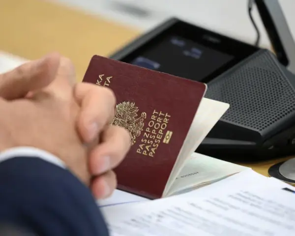 Pasport w rękach klienta w biurze paszportowym Myślibórz. Dokumenty i urządzenie do wideokonferencji na stole.