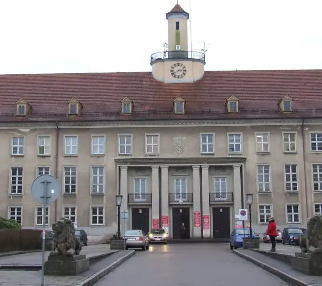 Elegancki budynek z zegarem na wieży, gdzie znajduje się urząd paszportowy Koszalin. Przed wejściem stoją lwy.