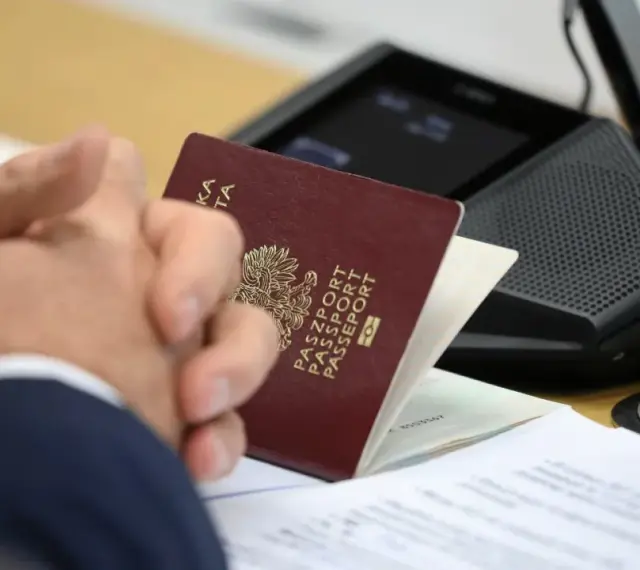 Pasport w rękach klienta w biurze paszportowym Myślibórz. Dokumenty i urządzenie do wideokonferencji na stole.