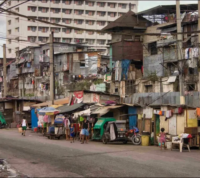 Uliczka w slumsach na Filipinach, gdzie życie toczy się wśród prowizorycznych domów i wszechobecnego prania. Czy w filipinach jest bezpiecznie? To pytanie nabiera nowego znaczenia w takich miejscach.
