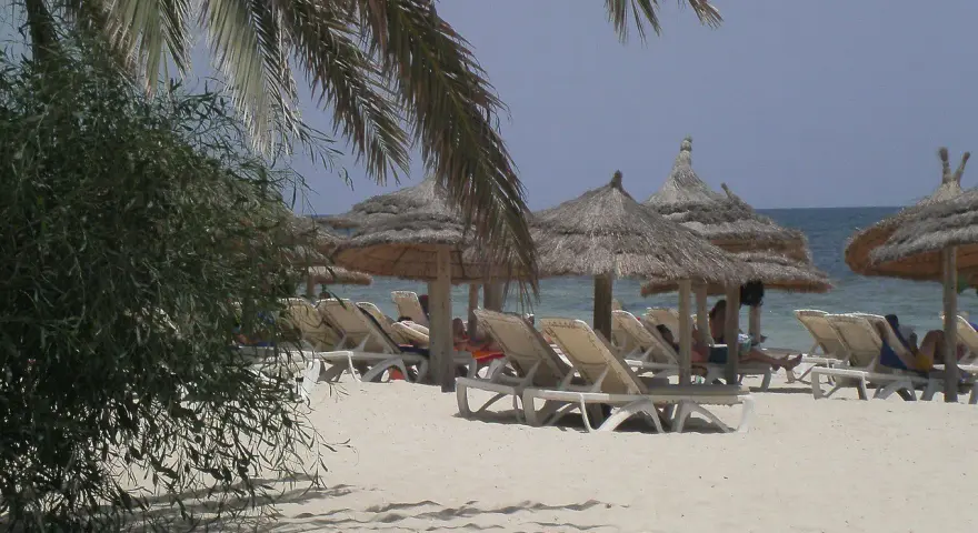 Plaża na Djerbie z leżakami i parasolami. Ludzie odpoczywają, co sugeruje, że na Djerbie jest bezpiecznie.