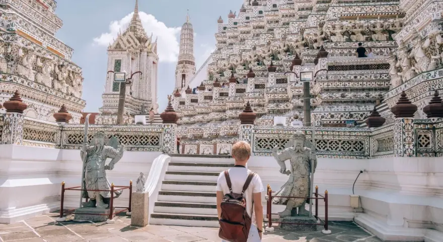 Młody turysta z plecakiem podziwia majestatyczną świątynię Wat Arun w Bangkoku. Czy Bangkok jest bezpieczny? Tak, zwłaszcza w takich pięknych i spokojnych miejscach.