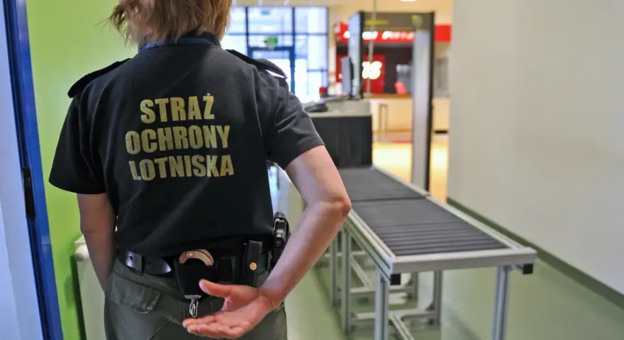 Ochroniarz lotniskowy przy taśmie bagażowej. Zastanawiasz się, czy można przewozić wódkę w bagażu rejestrowanym? Sprawdź przepisy!