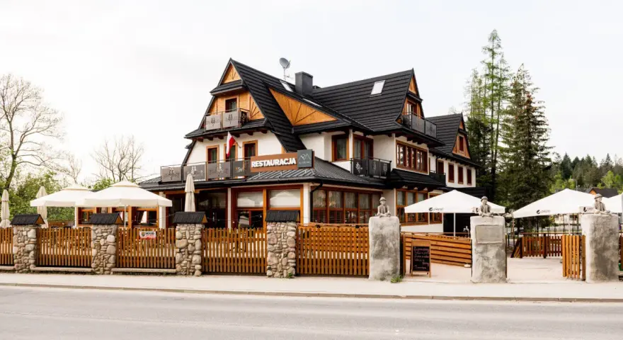 Szukasz miejsca, gdzie zjeść w Kościelisku? Ta restauracja z drewnianym ogrodzeniem i białymi parasolami zaprasza na góralskie smaki.