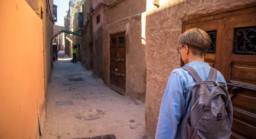 Młoda osoba z plecakiem idzie wąską uliczką w Marrakeszu. Czy w Marrakeszu jest bezpiecznie? Tak, zwiedzanie jest przyjemne.