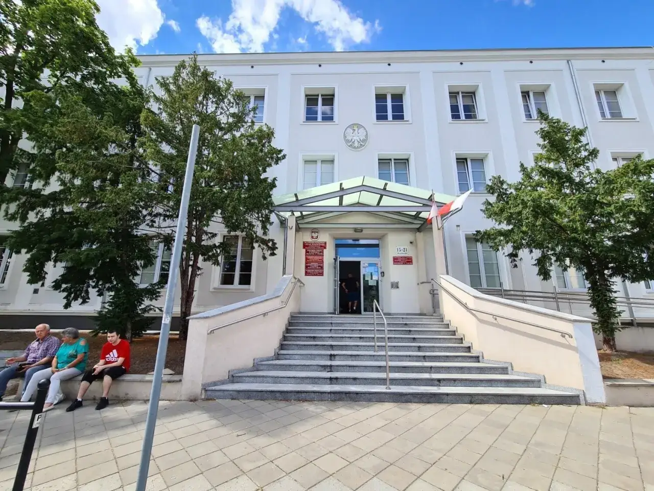 Urząd paszportowy Toruń. Wejście do budynku z szerokimi schodami i drzewami po bokach.