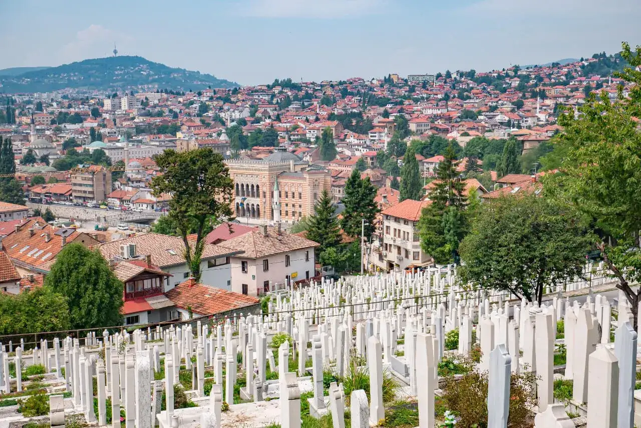 Widok na cmentarz w Sarajewie, z białymi nagrobkami i miastem w tle. Pytanie 
