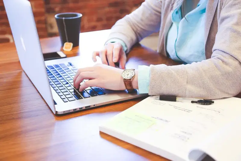 Kobieta pracuje na laptopie, szukając informacji, jak wyrobić paszport online. Na biurku leży notatnik i kubek z herbatą.